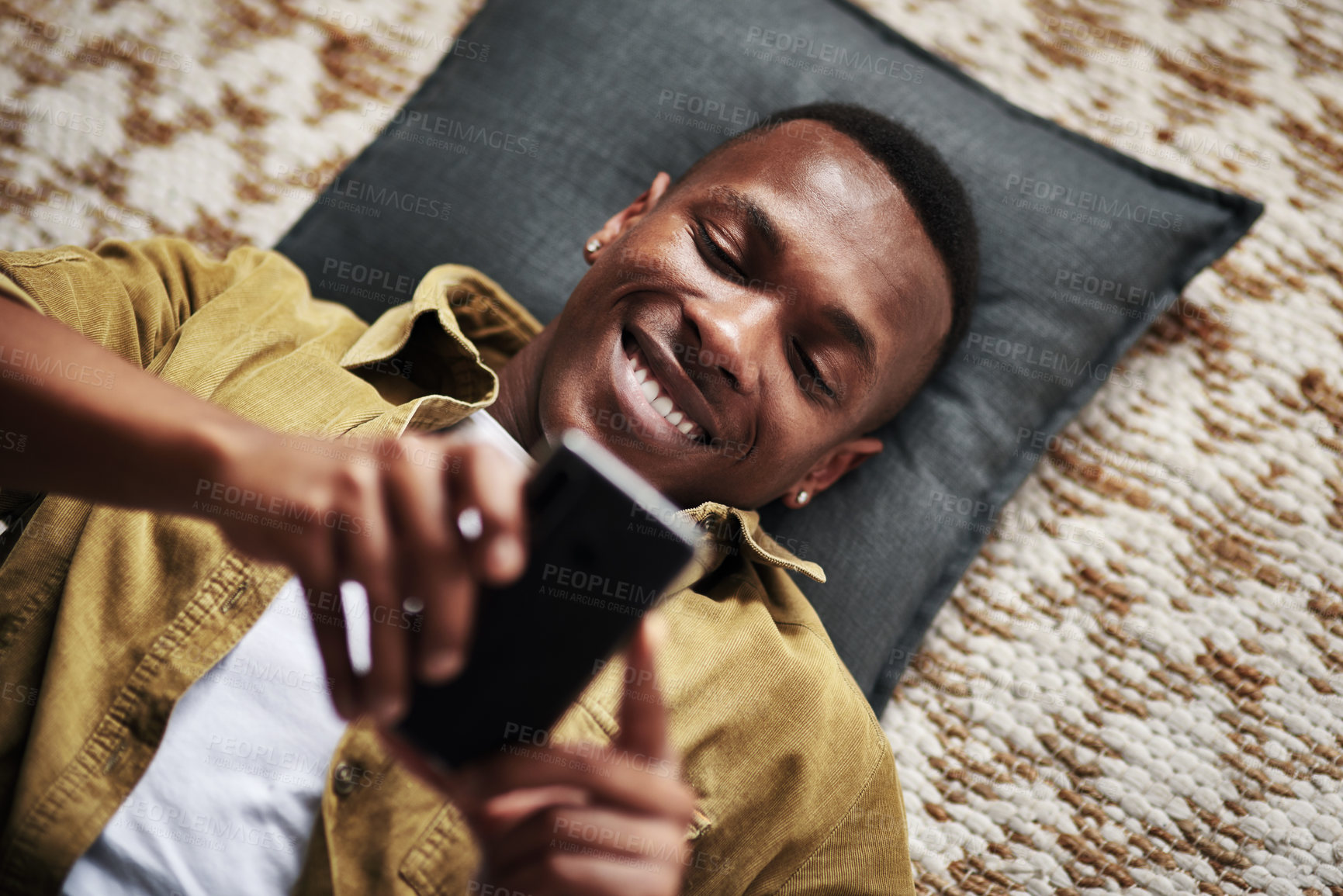 Buy stock photo Happy, black man and above with phone for social media, communication or online browsing on floor at home. Top view, young African or male person with smile on mobile smartphone for chat or texting