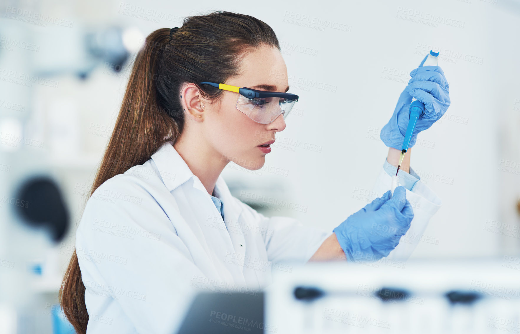 Buy stock photo Cropped shot of a focused young female scientist wearing protective glasses while pouring a test sample into a vile inside of a laboratory