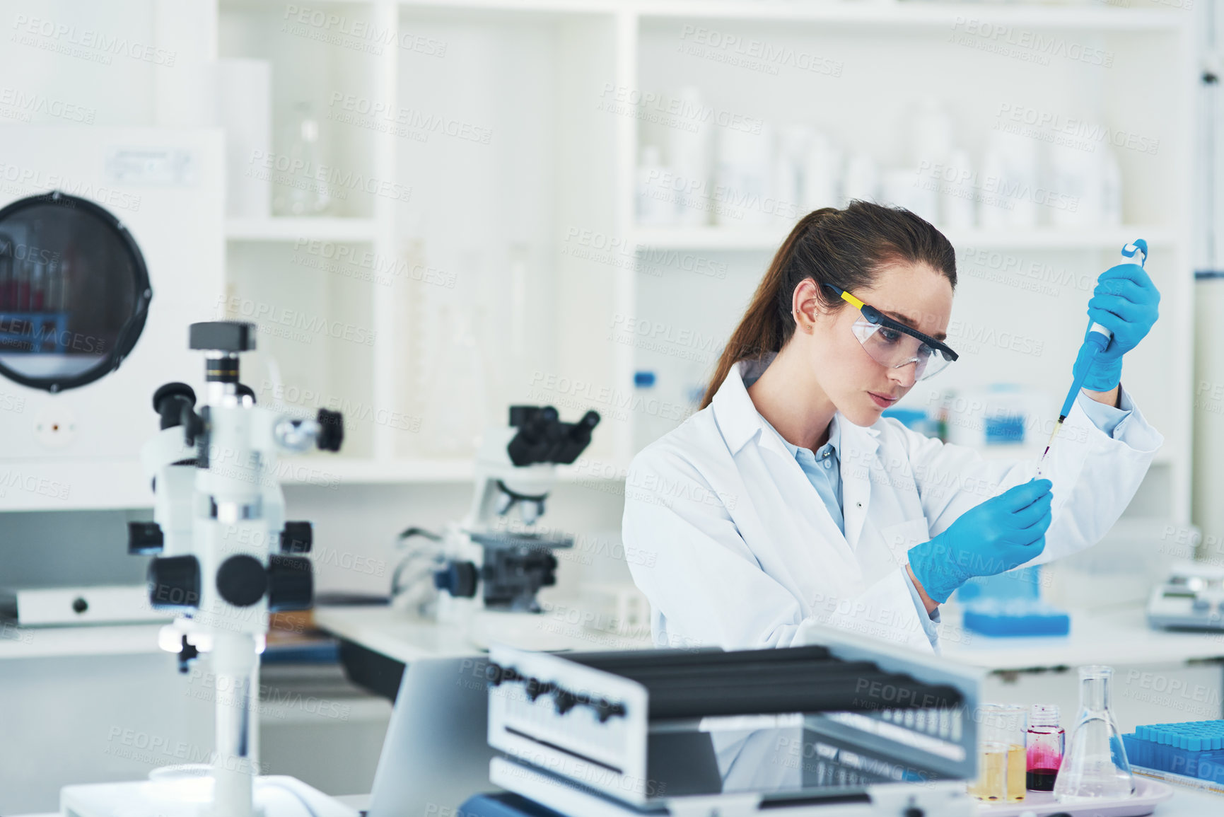 Buy stock photo Cropped shot of a focused young female scientist wearing protective glasses while pouring a test sample into a vile inside of a laboratory