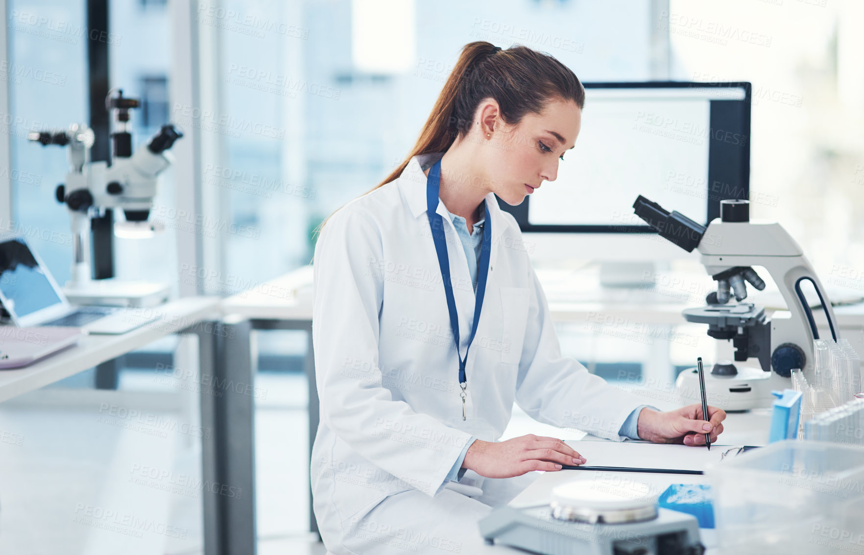 Buy stock photo Cropped shot of a focused young female scientist doing tests and making notes inside of a laboratory during the day