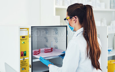 Buy stock photo Rearview shot of an unrecognizable young female scientist wearing protective fave gear while conducting experiments inside of a laboratory