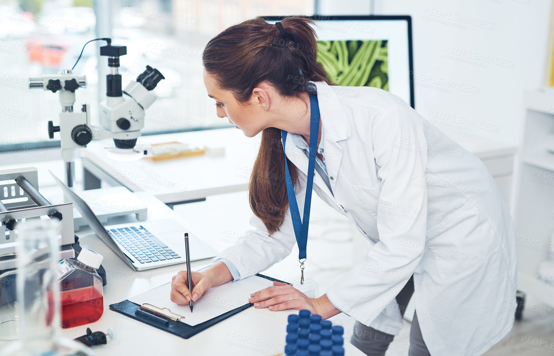 Buy stock photo Cropped shot of a focused young female scientist making notes in a book while doing tests inside of a laboratory during the day