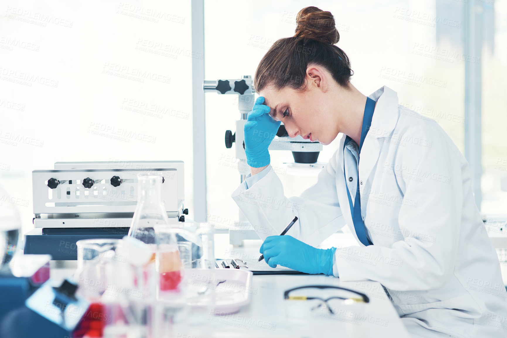 Buy stock photo Cropped shot of a tired young female scientist making notes while conducting experiments inside of a laboratory during the day