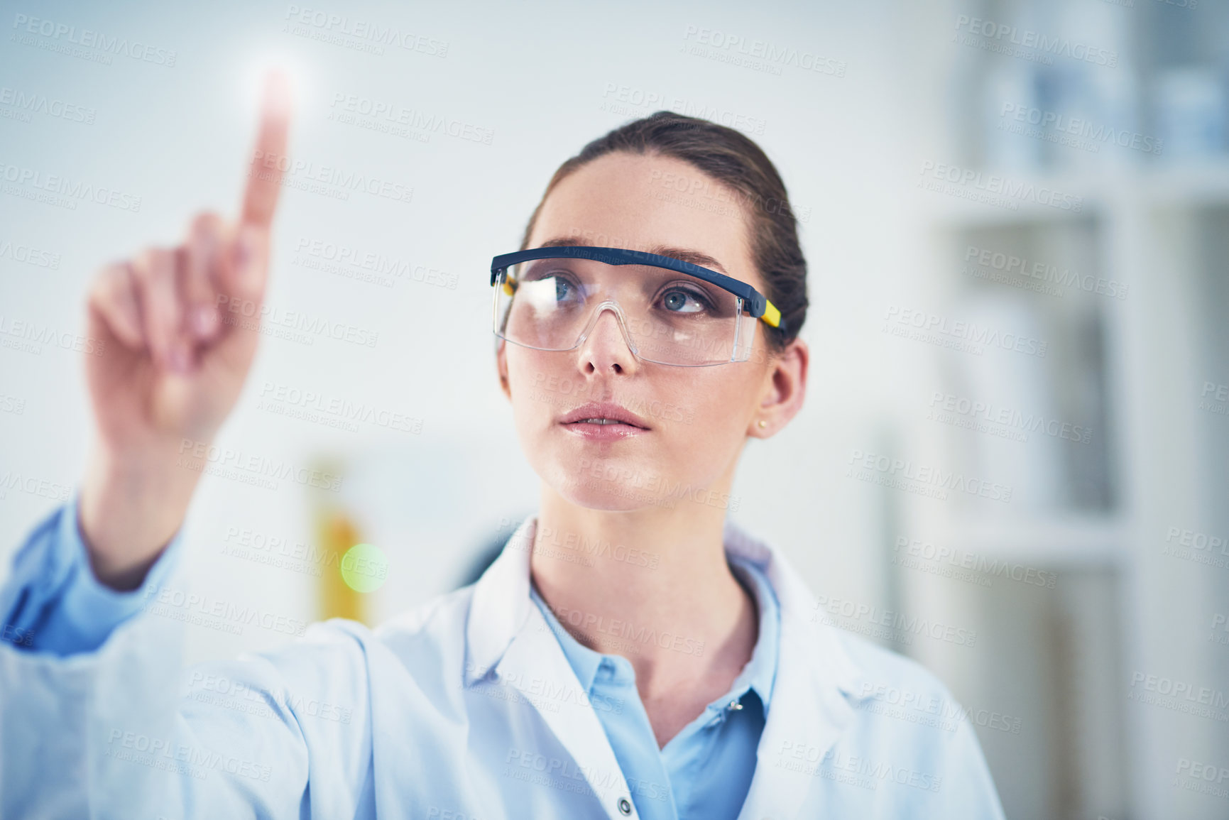 Buy stock photo Cropped shot of a focused young female scientist wearing protective glasses while pointing with her finger on a glass wall