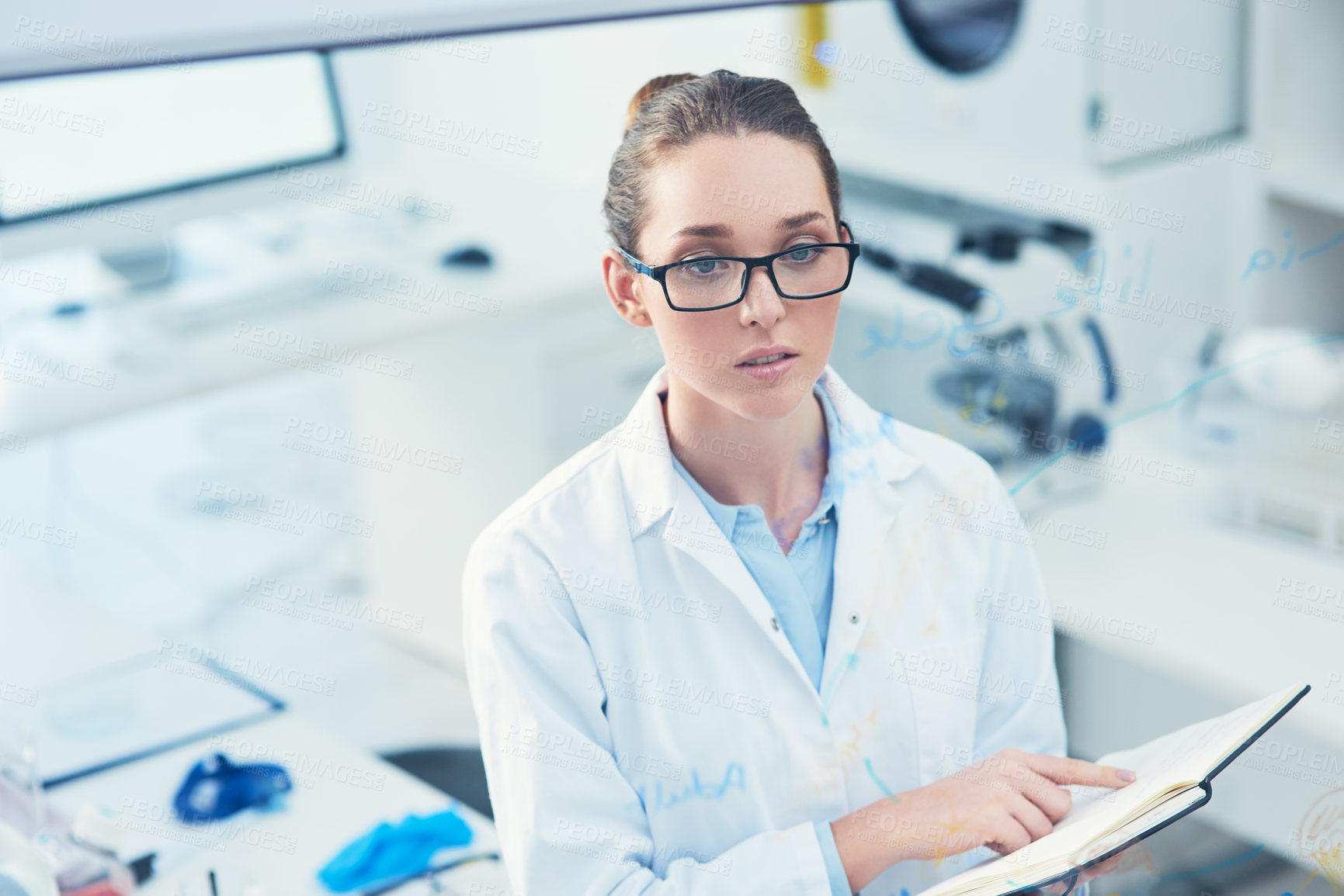 Buy stock photo Portrait of a focused young female scientist reading from her notebook inside of a laboratory