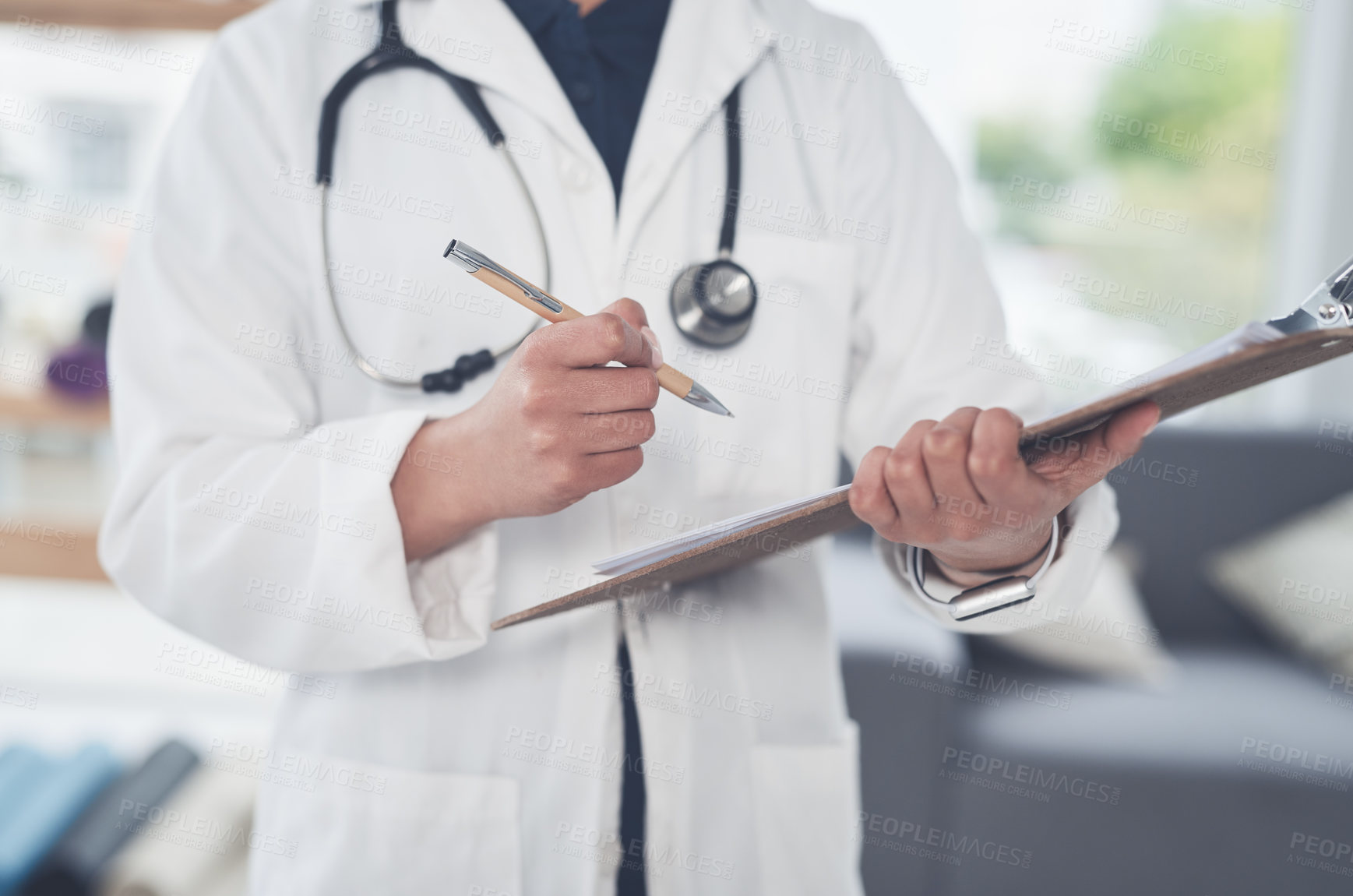 Buy stock photo Cropped shot of an unrecognizable female doctor writing on a clipboard while standing in her office