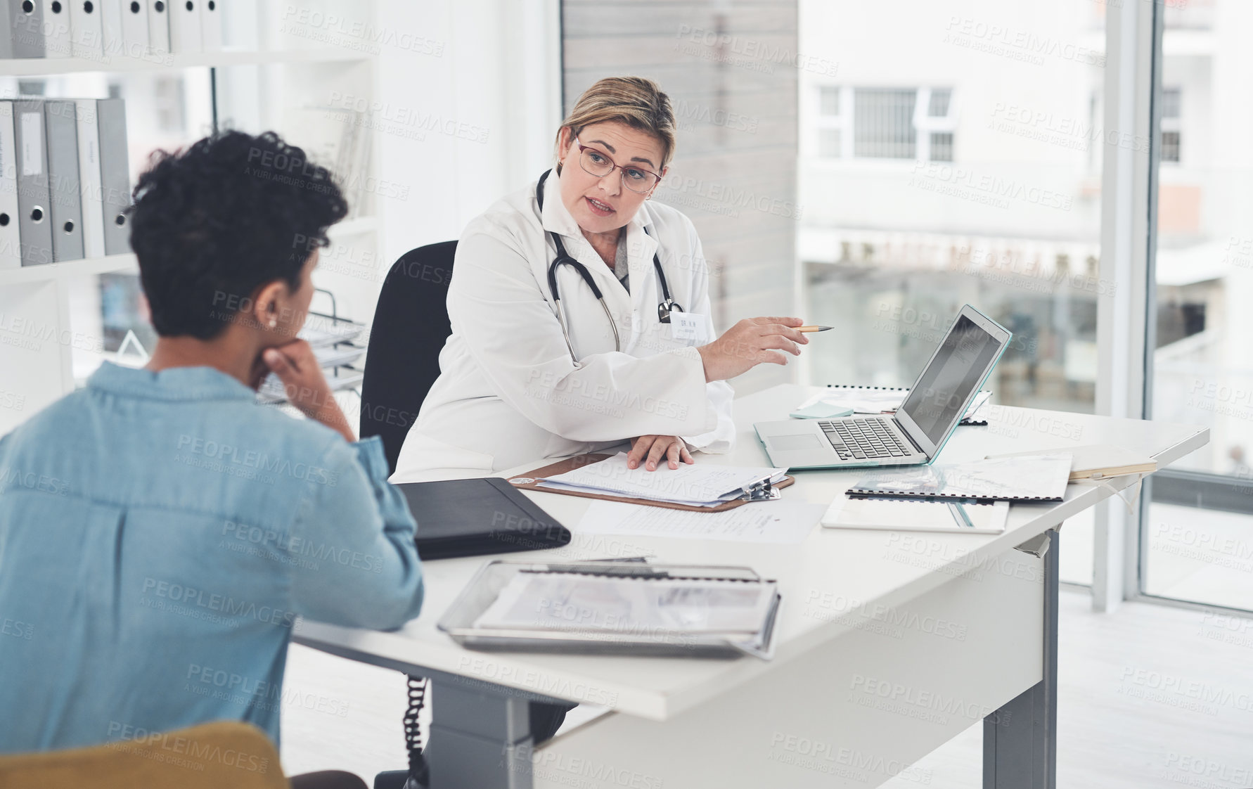 Buy stock photo Cropped shot of an attractive young female doctor using a laptop while having a discussion with a female patient in her office