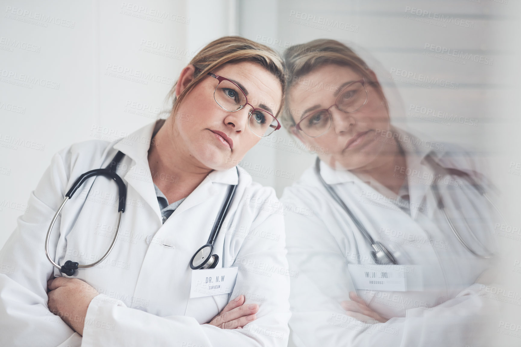 Buy stock photo Cropped shot of an attractive young female doctor looking thoughtful while leaning against the wall with her arms crossed in her office