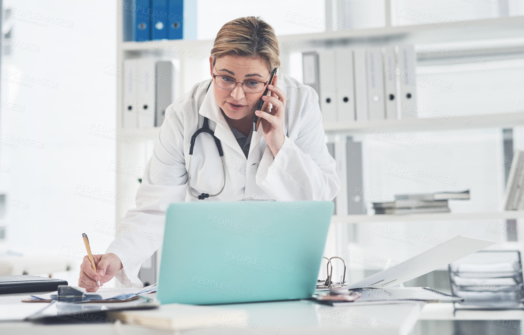 Buy stock photo Cropped shot of an attractive young female doctor writing on a clipboard while taking a phonecall in her office