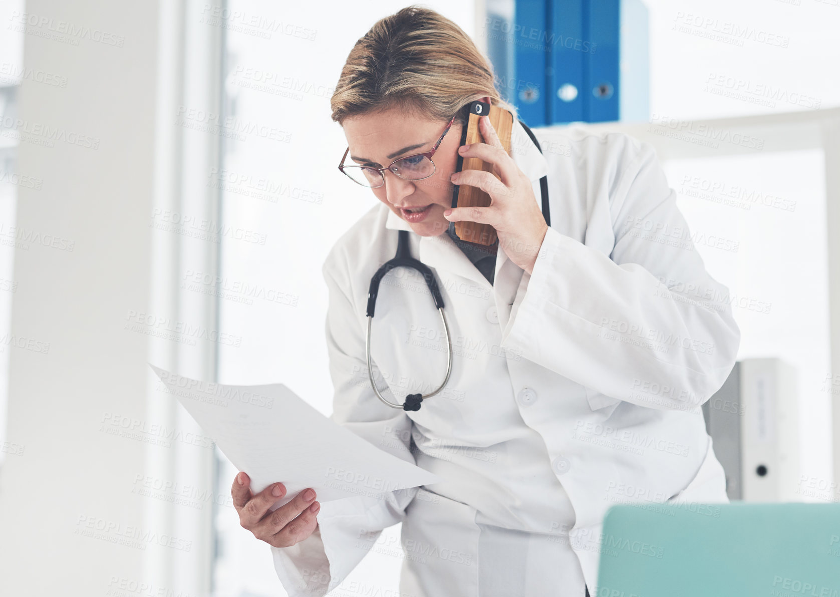 Buy stock photo Cropped shot of an attractive young female doctor looking at a document while taking a phonecall in her office