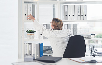 Buy stock photo Rearview shot of an unrecognizable female doctor reaching over to take a file while working in her office