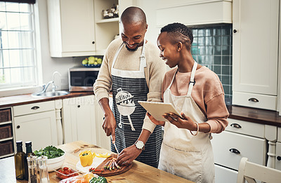 Buy stock photo Cropped shot of an affectionate young couple using a tablet while preparing dinner in their kitchen