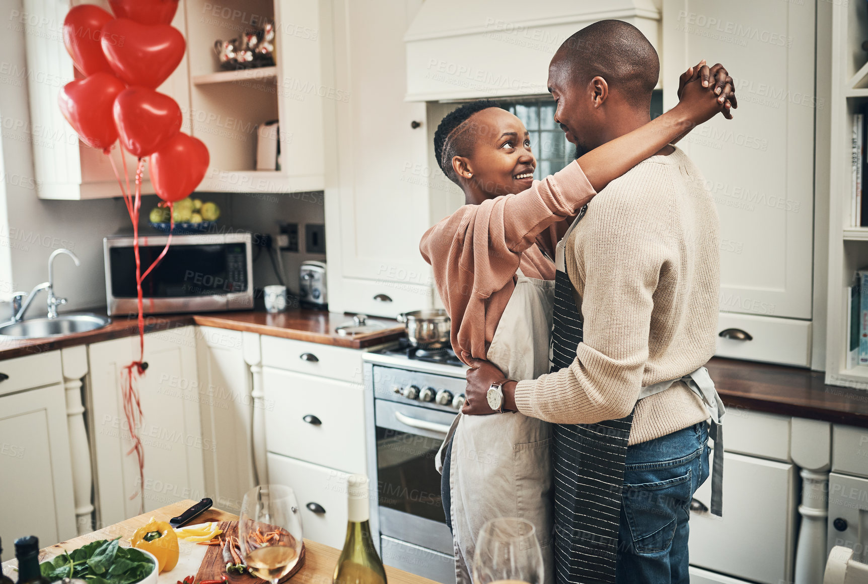Buy stock photo Cropped shot of an affectionate young couple embracing while preparing dinner in their kitchen