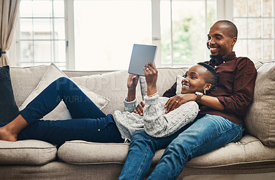 Buy stock photo Shot of a happy young couple using a digital tablet while relaxing together at home