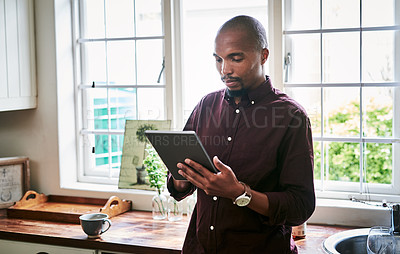 Buy stock photo Shot of a handsome young businessman using a digital tablet while working from home during the day