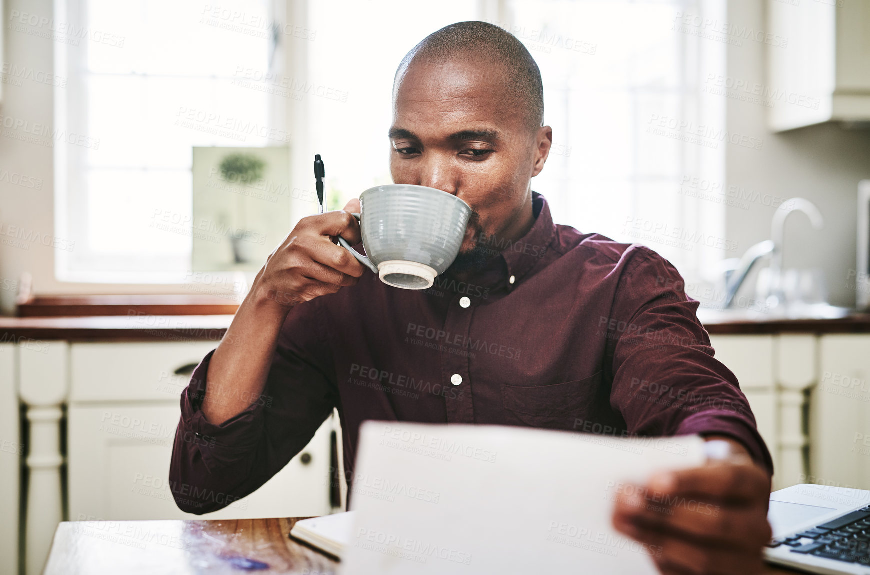 Buy stock photo Shot of a handsome young man drinking coffee and going over paperwork at home