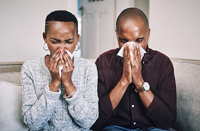Buy stock photo Shot of a sickly young couple blowing their noses with tissues at home
