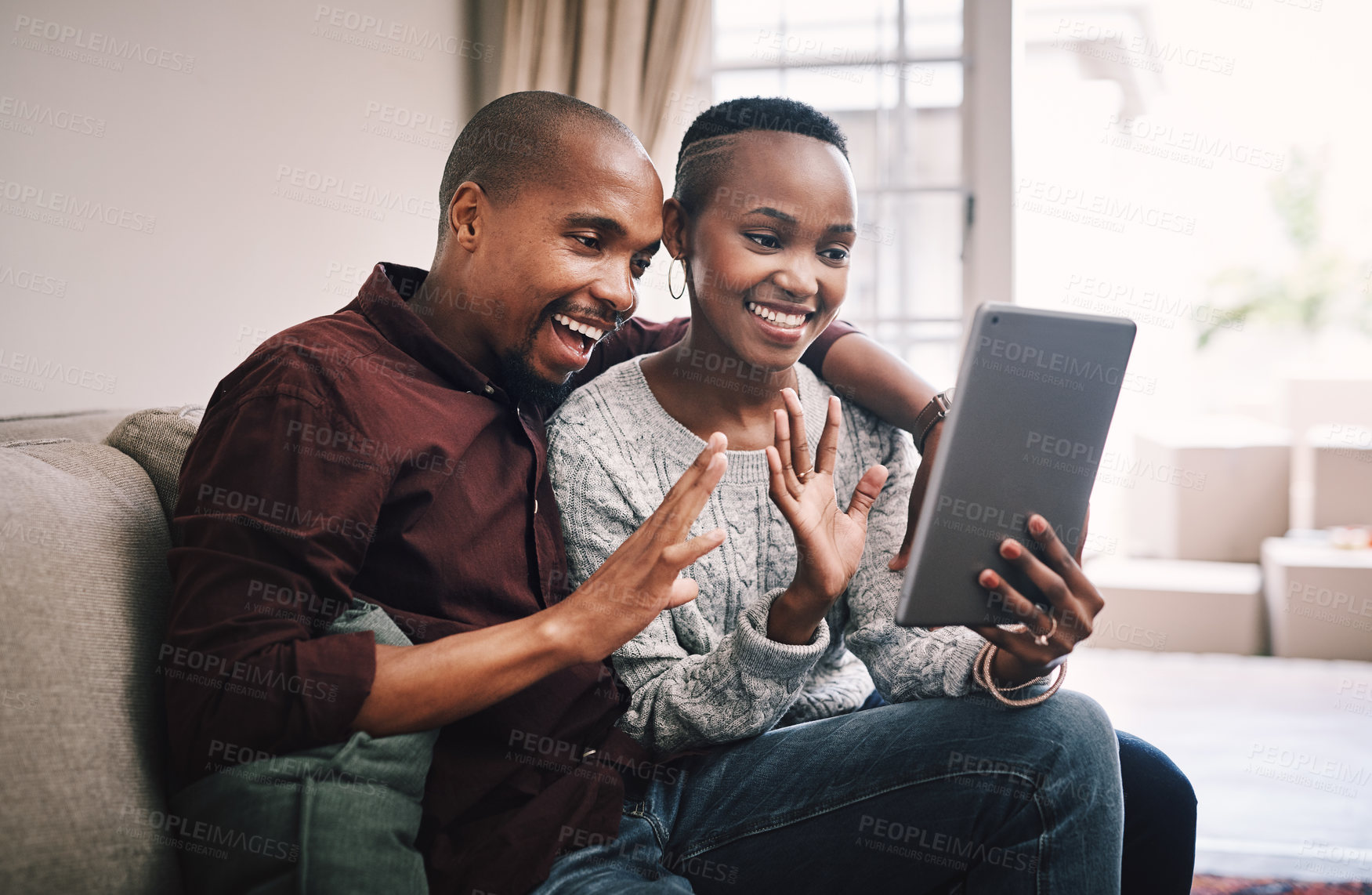 Buy stock photo Shot of a happy young couple using their digital tablet to make a video call while relaxing together at home