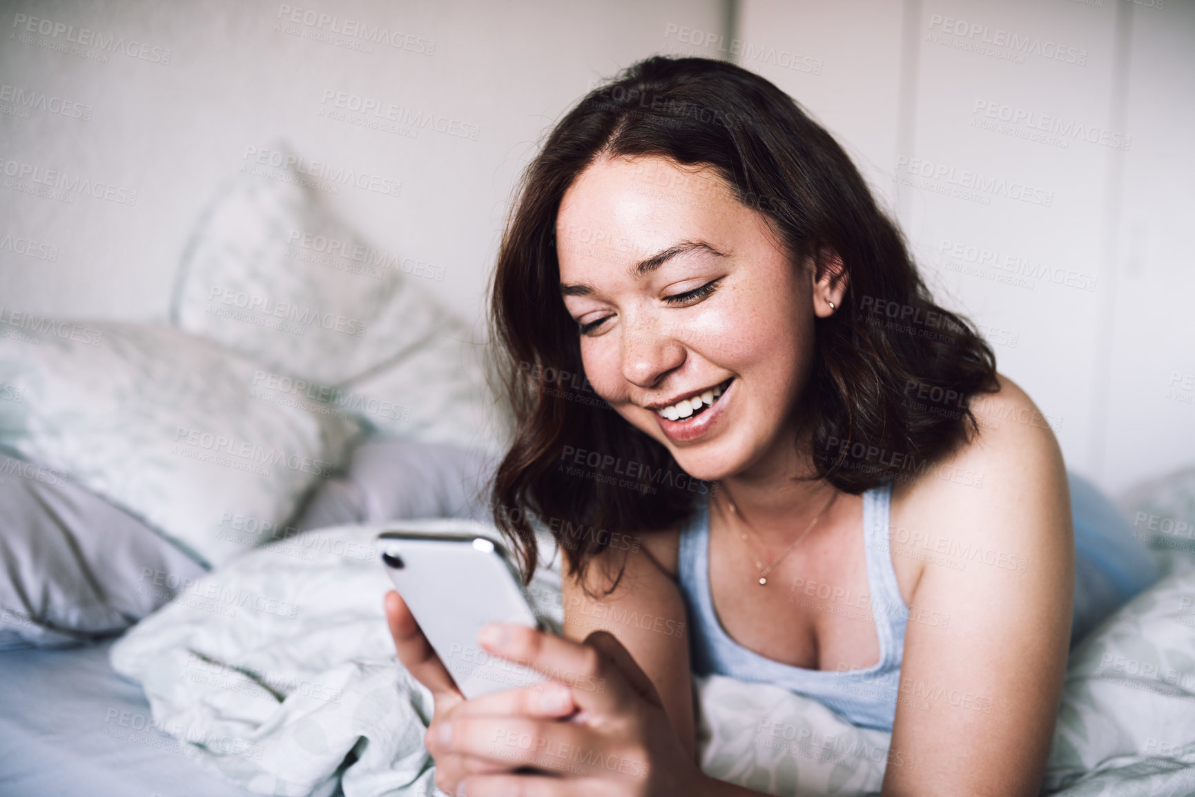 Buy stock photo Shot of an attractive young woman smiling while using a smartphone in her bedroom at home