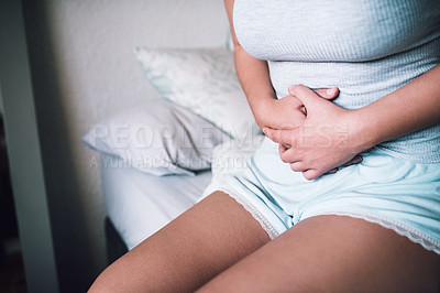 Buy stock photo Cropped shot of an unrecognizable woman suffering with stomach cramps while sitting on her bed at home