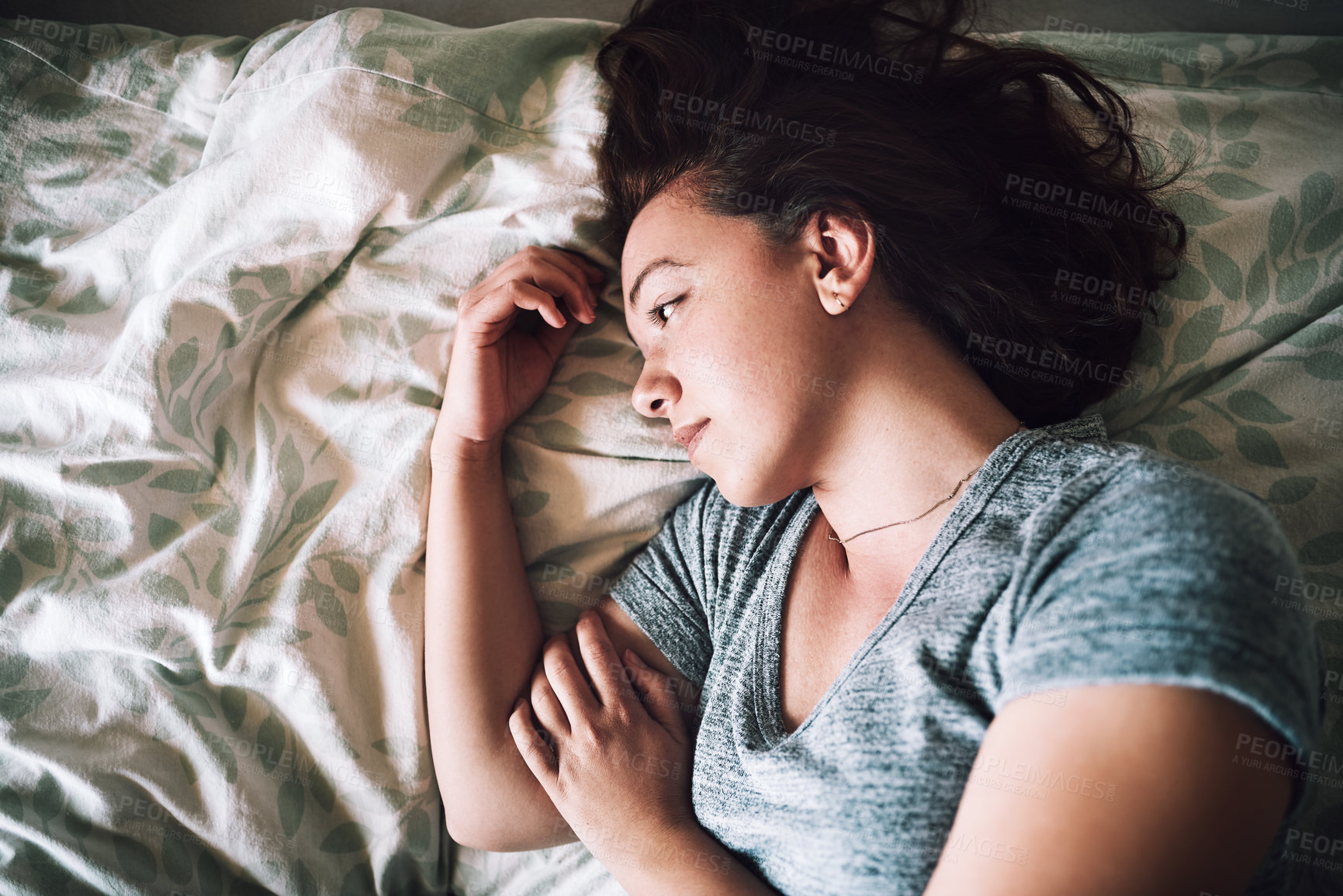 Buy stock photo High angle shot of an attractive young woman looking depressed while lying on her bed at home
