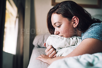 Buy stock photo Cropped shot of an attractive young woman looking depressed while lying on her bed at home