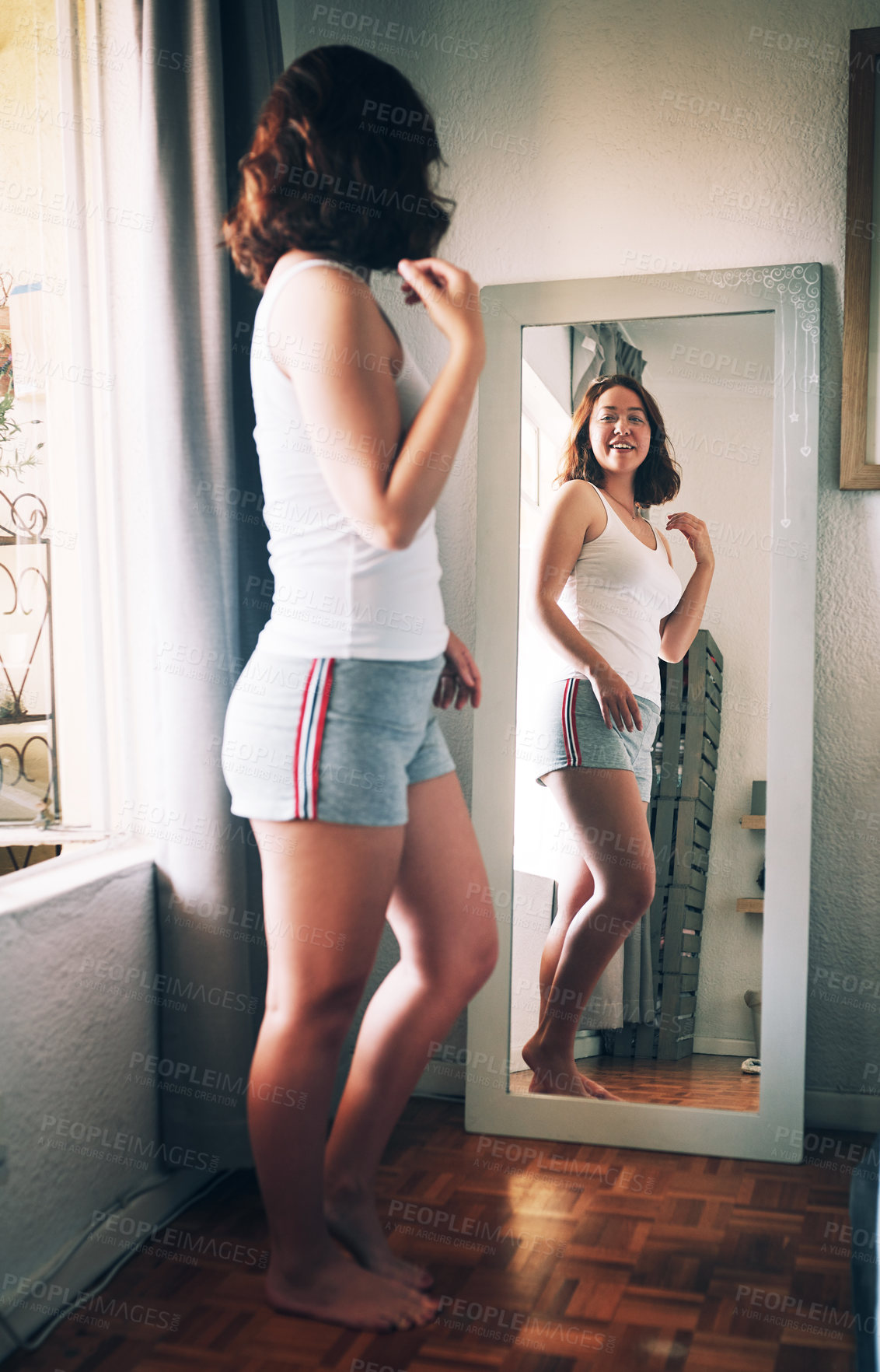 Buy stock photo Full length shot of an attractive young woman admiring herself while standing in front of the mirror in her bedroom at home