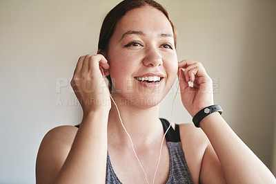 Buy stock photo Cropped shot of an attractive young woman standing alone and listening to music through earphones before her workout at home