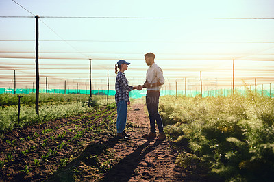 Buy stock photo Full length shot of two young farmers shaking hands while working on their farm
