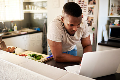 Buy stock photo Cropped shot of a handsome young man using a digital tablet while making breakfast in his kitchen at home