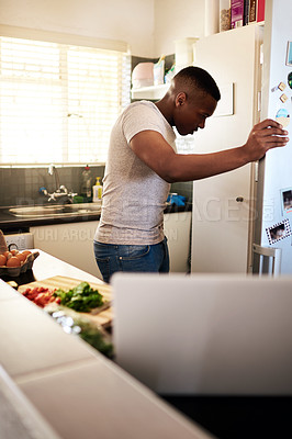 Buy stock photo Cropped shot of a handsome young man looking into his refrigerator while making breakfast in his kitchen at home