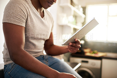 Buy stock photo Cropped shot of an unrecognizable man using a digital tablet while sitting on the kitchen counter at home