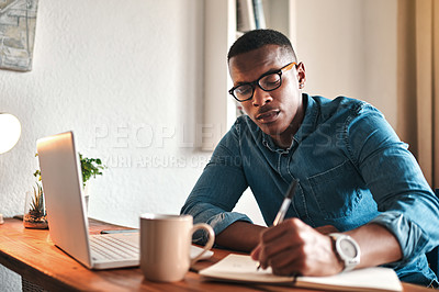 Buy stock photo Cropped shot of a handsome young businessman sitting alone in his home office and writing notes