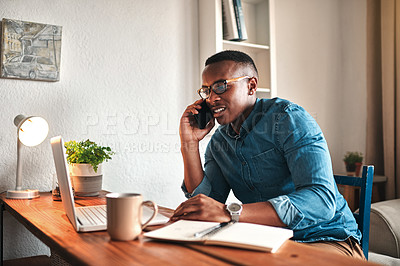 Buy stock photo Cropped shot of a handsome young businessman sitting alone in his home office and talking on his cellphone
