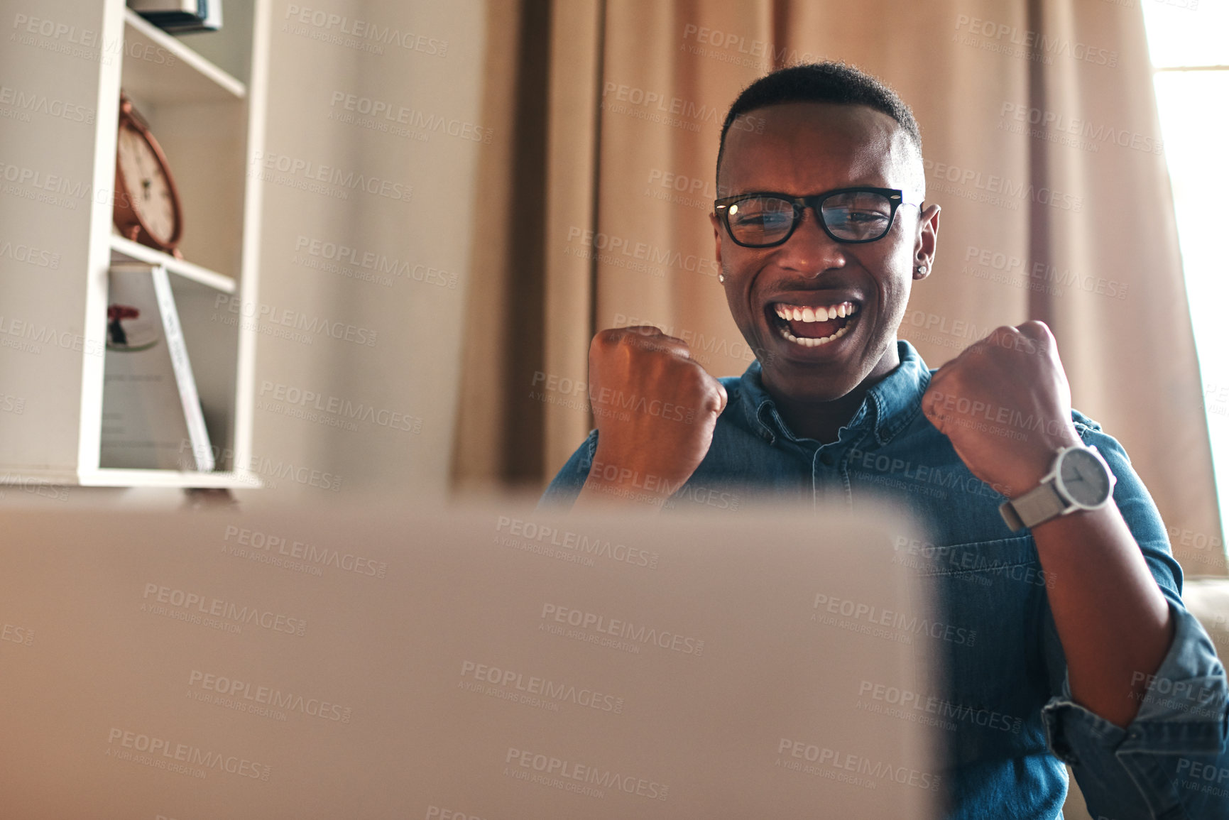 Buy stock photo Cropped shot of a handsome young businessman sitting alone in his home office and feeling excited while using his laptop