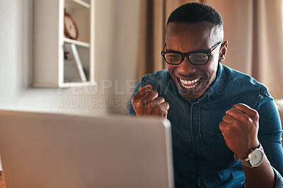 Buy stock photo Cropped shot of a handsome young businessman sitting alone in his home office and feeling excited while using his laptop