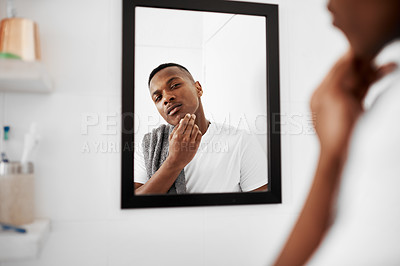 Buy stock photo Cropped shot of a young man touching his face while looking into the bathroom mirror