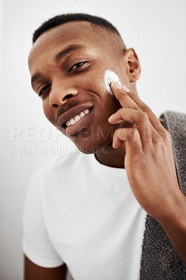 Buy stock photo Shot of a handsome young man applying moisturizer to his face at home