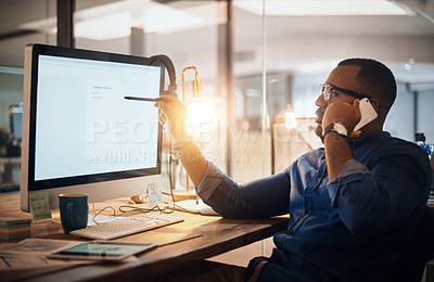 Buy stock photo Shot of a young businessman talking on a cellphone while working on a computer in an office at night