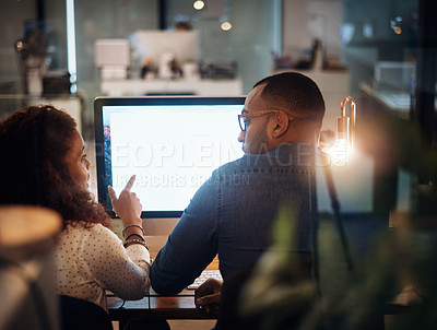Buy stock photo Rearview shot of two businesspeople working together on a computer in an office at night