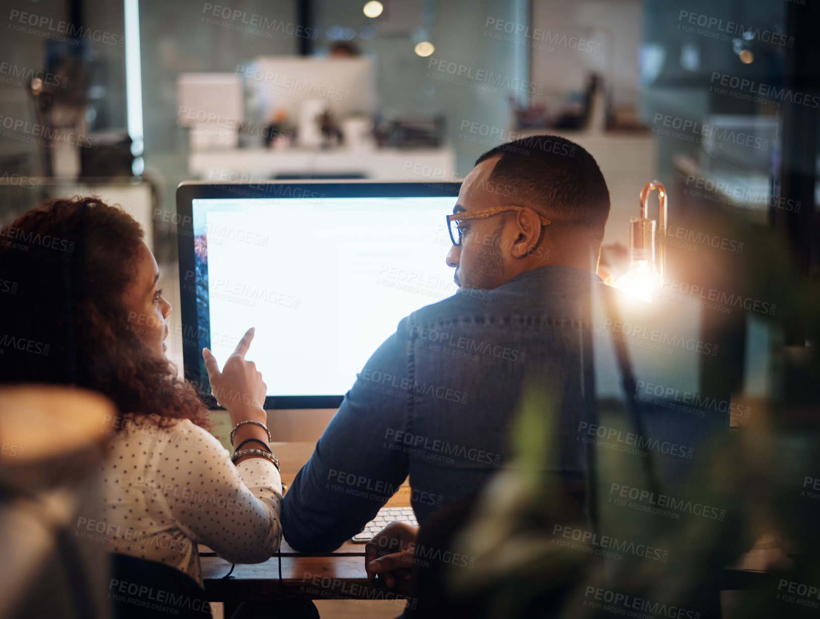 Buy stock photo Rearview shot of two businesspeople working together on a computer in an office at night