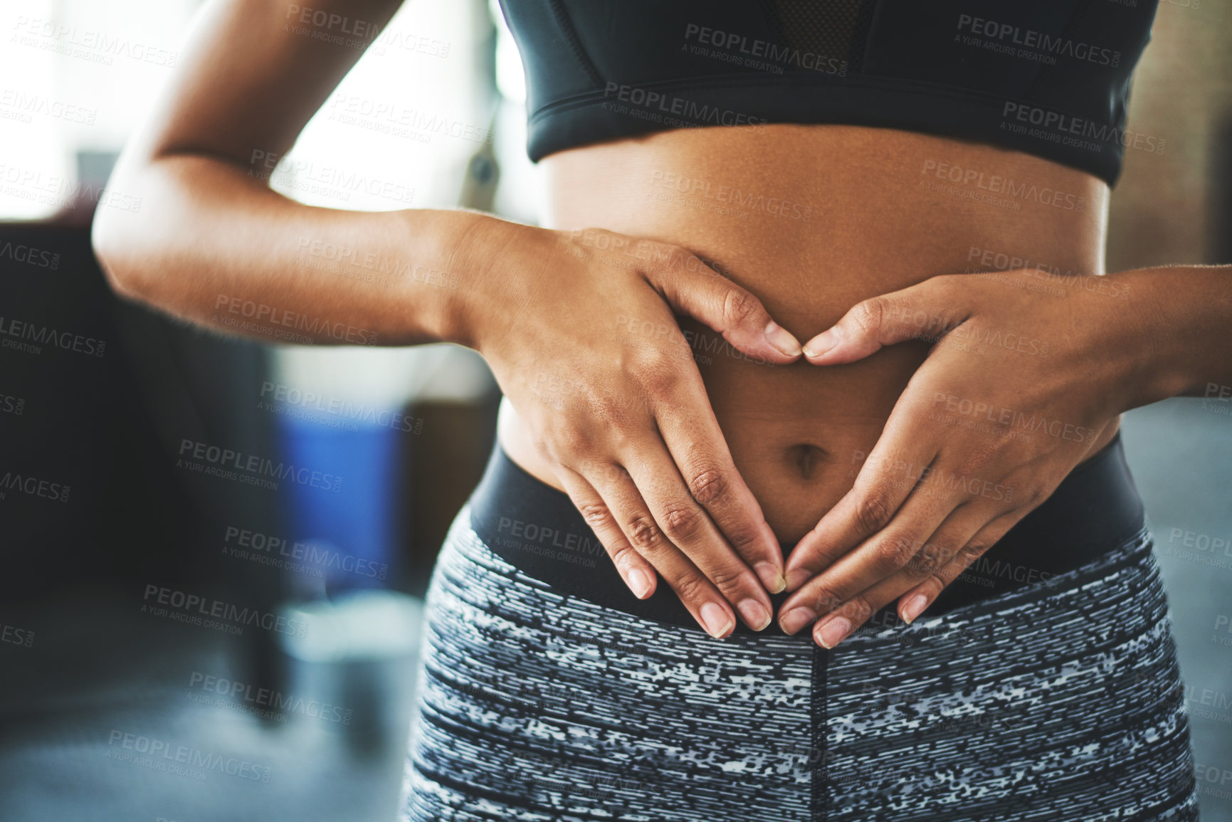 Buy stock photo Cropped shot of a fit young woman making a heart shaped gesture over her stomach in a gym