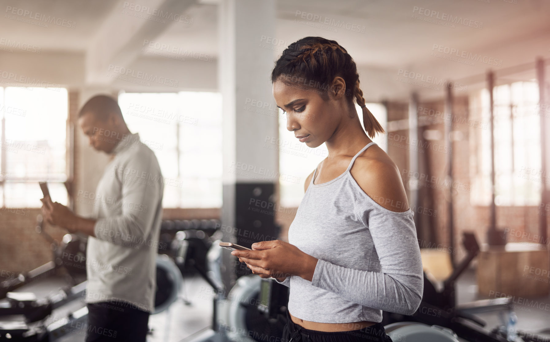 Buy stock photo Shot of a young woman using their smartphones in a gym