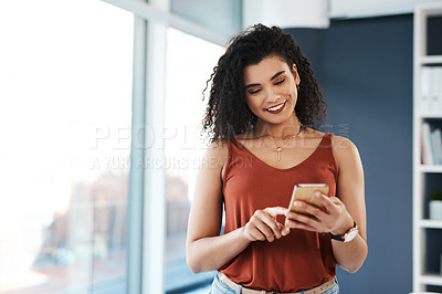 Buy stock photo Cropped shot of an attractive young businesswoman standing alone in her office and texting on her cellphone