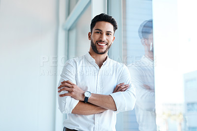 Buy stock photo Cropped portrait of a handsome young businessman standing with his arms folded in his office alone