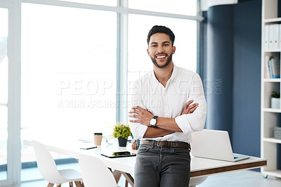 Buy stock photo Cropped portrait of a handsome young businessman sitting with his arms folded in his office alone