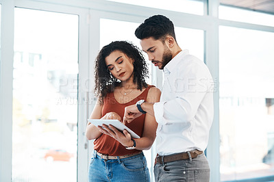 Buy stock photo Cropped shot of two young business colleagues standing together in the office and using a tablet