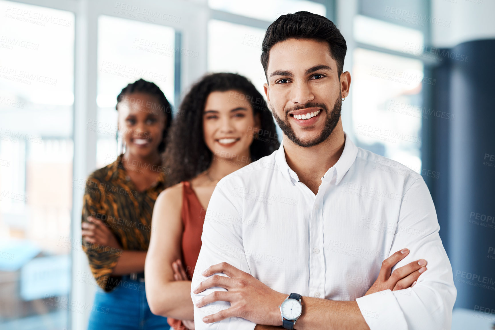 Buy stock photo Cropped portrait of a handsome young businessman standing with his arms crossed in front of his colleagues in the office