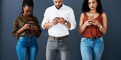 Buy stock photo Cropped shot of a diverse group of businesspeople standing against a gray background in the studio and using their cellphones
