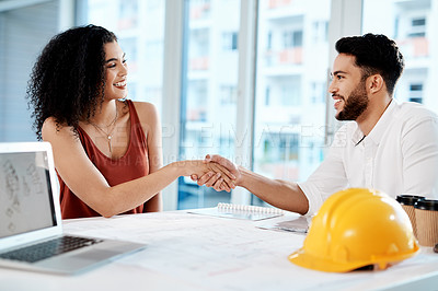 Buy stock photo Cropped shot of two young businesspeople sitting together and shaking hands in agreement with building renovation plans
